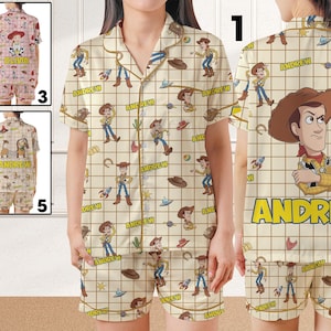 May include: A short-sleeved button-down pajama shirt and matching shorts set featuring a beige grid pattern with repeating Woody character graphics, cowboy hats, and the name ANDREW printed in yellow block letters throughout the fabric.