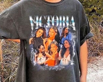 May include: Dark gray oversized t-shirt featuring the name "Victoria" in a stylized font above a collage of women's portraits. The design includes lightning bolt accents and a vintage aesthetic.