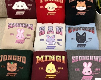 Puede incluir: Una colección de sudaderas coloridas con personajes de animales de dibujos animados y nombres en una fuente universitaria. Cada sudadera tiene un color diferente, incluyendo burdeos, rojo, negro, beige, blanco, azul claro, verde oscuro y gris.