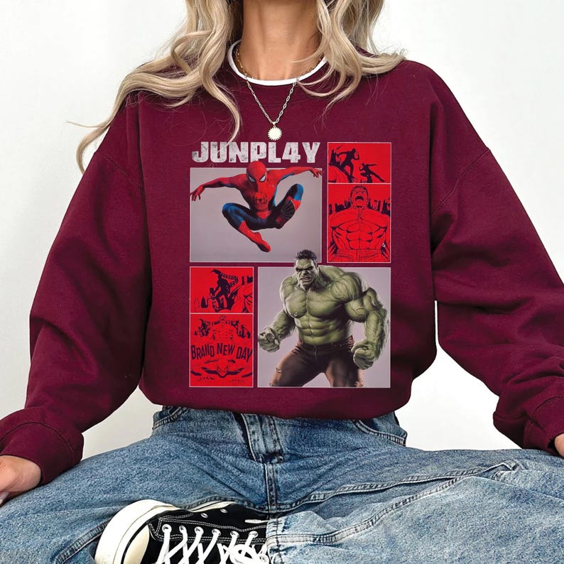 Op de afbeelding: Bordeaux sweatshirt met een grafisch ontwerp met de tekst "JUNPLAY" en afbeeldingen van Spider-Man en Hulk. Het ontwerp bevat rode panelen met illustraties en de tekst "BRAND NEW DAY".