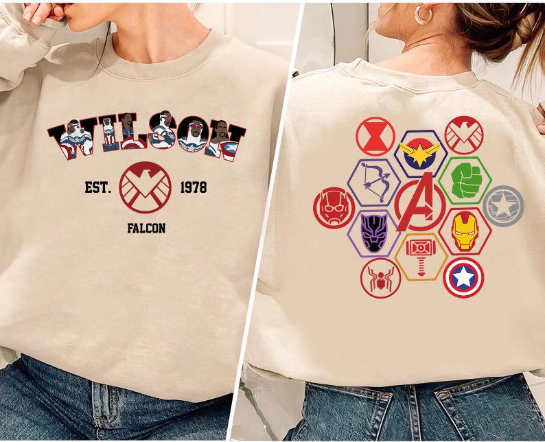 Puede incluir: Sudadera beige con la palabra "WILSON" en estilo c&oacute;mic, con ilustraciones de personajes. Debajo, un logotipo de escudo rojo con "EST. 1978 FALCON". La parte trasera muestra varios logotipos de superh&eacute;roes en formas hexagonales coloridas.