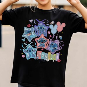 Może przedstawiać: Czarny t-shirt z kolorową grafiką postaci Stitch z Lilo & Stitch. Stitch jest przedstawiony w ramkach w kształcie gwiazd z kokardkami, balonami i napisem "magical". Projekt zawiera serca, kwiaty i balon w kształcie Myszki Miki.