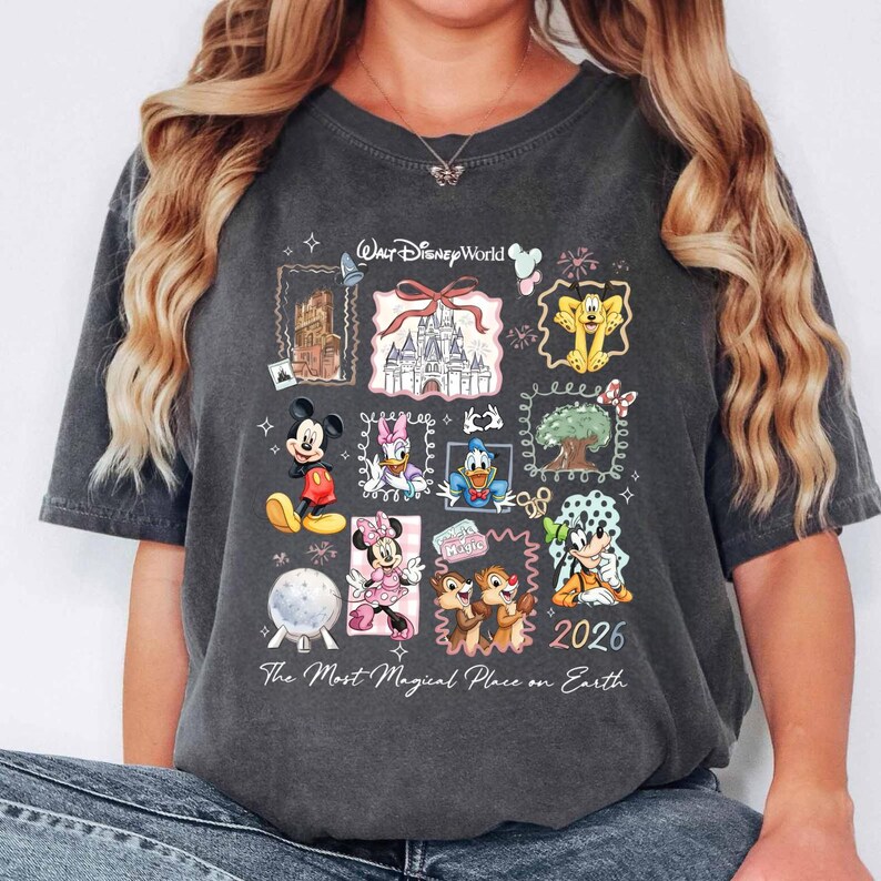 Puede incluir: Camiseta gris oscuro con un colorido collage de personajes y lugares de Disney. El dise&ntilde;o incluye a Mickey Mouse, Minnie Mouse, el Pato Donald y Chip y Chop, con los textos "Walt Disney World" y "2026". La frase "The Most Magical Place on Earth" tambi&eacute;n est&aacute; impresa.