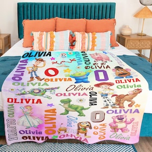 Op de afbeelding: Een zachte fleece deken met een kleurrijke print van diverse Toy Story-personages, waaronder Woody, Buzz Lightyear, Jessie en Rex. Het ontwerp bevat de naam Olivia, herhaald in verschillende lettertypes en kleuren op een witte achtergrond.