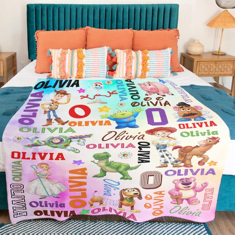 Op de afbeelding: Een zachte fleece deken met een kleurrijke print van diverse Toy Story-personages, waaronder Woody, Buzz Lightyear, Jessie en Rex. Het ontwerp bevat de naam Olivia, herhaald in verschillende lettertypes en kleuren op een witte achtergrond.