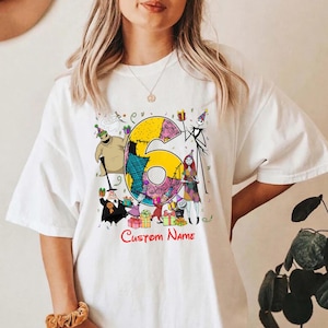 May include: A white t-shirt featuring a large yellow number six decorated with patchwork patterns. The design includes various animated characters from The Nightmare Before Christmas, colorful gift boxes, and the red text Custom Name.