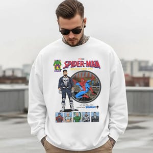 May include: White sweatshirt featuring a comic book-style graphic of Spider-Man, The Punisher, and Hulk. The graphic includes the text "SPIDER-MAN BRAND NEW DAY" and other comic book elements. The sweatshirt is a crew neck style.