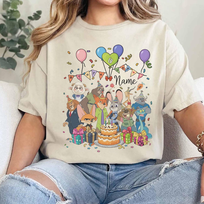 Puede incluir: Camiseta beige con un dise&ntilde;o de cumplea&ntilde;os colorido. Presenta personajes de dibujos animados, globos, confeti, una tarta y la palabra "Name". El dise&ntilde;o incluye una pancarta que dice "Birthday".
