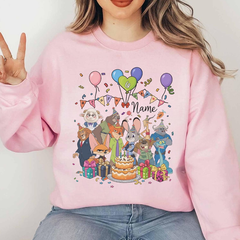 Puede incluir: Sudadera rosa claro con un dise&ntilde;o de fiesta de cumplea&ntilde;os colorido. Presenta personajes de dibujos animados, globos, confeti y una tarta de dos pisos. El dise&ntilde;o incluye el n&uacute;mero 6 y la palabra "Name".