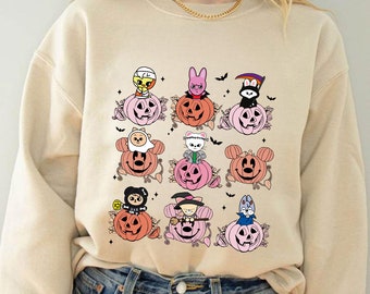 May include: Beige sweatshirt featuring a grid of cartoon characters atop pink and orange pumpkins. Each pumpkin has a jack-o'-lantern face. Black bats and floral accents surround the pumpkins, creating a Halloween theme.