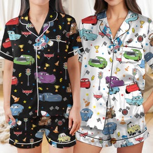 Può includere: Due set di pigiami a maniche corte con bottoni, composti da camicia e pantaloncini, con un motivo ripetuto di personaggi del film Cars, tra cui auto da corsa, semafori, trofei e bandiere a scacchi, nelle varianti di colore nero e bianco.