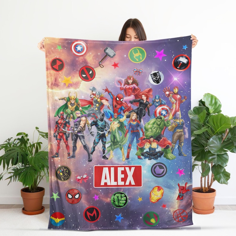May include: A rectangular fleece blanket featuring a vibrant space-themed background with numerous Marvel superhero characters, including Spider-Man, Thor, and Hulk. The center displays a red rectangular label with the white text ALEX.