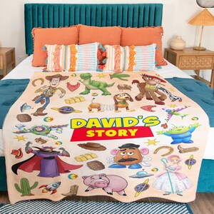 Puede incluir: Una manta de forro polar beige con un estampado colorido de personajes de Toy Story, incluyendo a Woody, Buzz Lightyear, Rex y el Sr. Patata, con el texto "DAVID'S STORY" impreso en grandes letras amarillas y rojas en el centro de la tela.