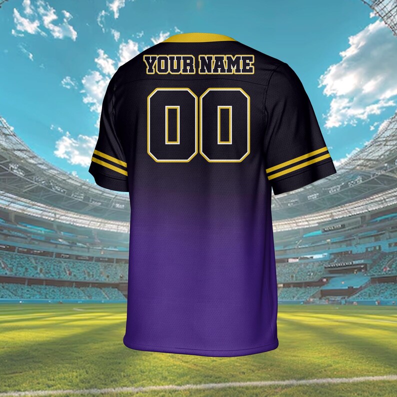 Puede incluir: Camiseta negra y morada con detalles dorados. La camiseta presenta el texto "YOUR NAME" sobre el n&uacute;mero "00" en dorado. Rayas doradas adornan las mangas. La camiseta se muestra en un estadio.