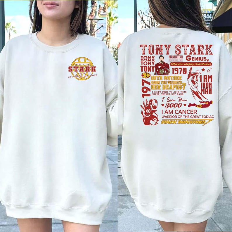 May include: Cream-colored sweatshirt with a front chest graphic of the Stark Industries logo and text. The back features a red graphic with the text "Tony Stark" and other phrases, including "I am Iron Man."