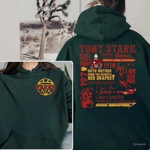 May include: Dark green hoodie featuring the text "TONY STARK" and various phrases and graphics in red and yellow. The hoodie includes the text "STARK INDUSTRIES" and a graphic of the Iron Man suit. The front of the hoodie has a logo.