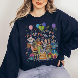 Puede incluir: Sudadera azul marino con un gr&aacute;fico de dibujos animados colorido de varios personajes de animales, globos, confeti y una tarta de cumplea&ntilde;os. El gr&aacute;fico incluye el n&uacute;mero 6 y la palabra "Name". Tambi&eacute;n se ven varios regalos envueltos.