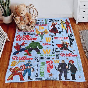May include: A light blue blanket featuring various Marvel superhero characters, including Spider-Man, Hulk, and Captain America. The blanket has the name "William" printed in multiple locations, along with stars and the letter "W".