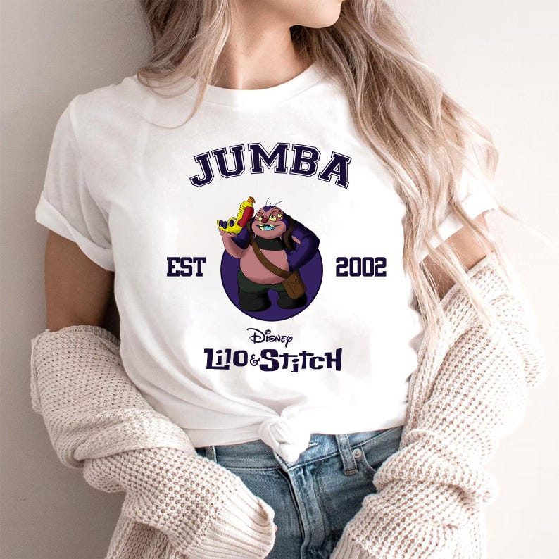 May include: White t-shirt featuring a graphic of Jumba from Disney's Lilo & Stitch. The design includes the text "JUMBA", "EST 2002", and the Disney Lilo & Stitch logo. Jumba is depicted holding a yellow and red weapon.