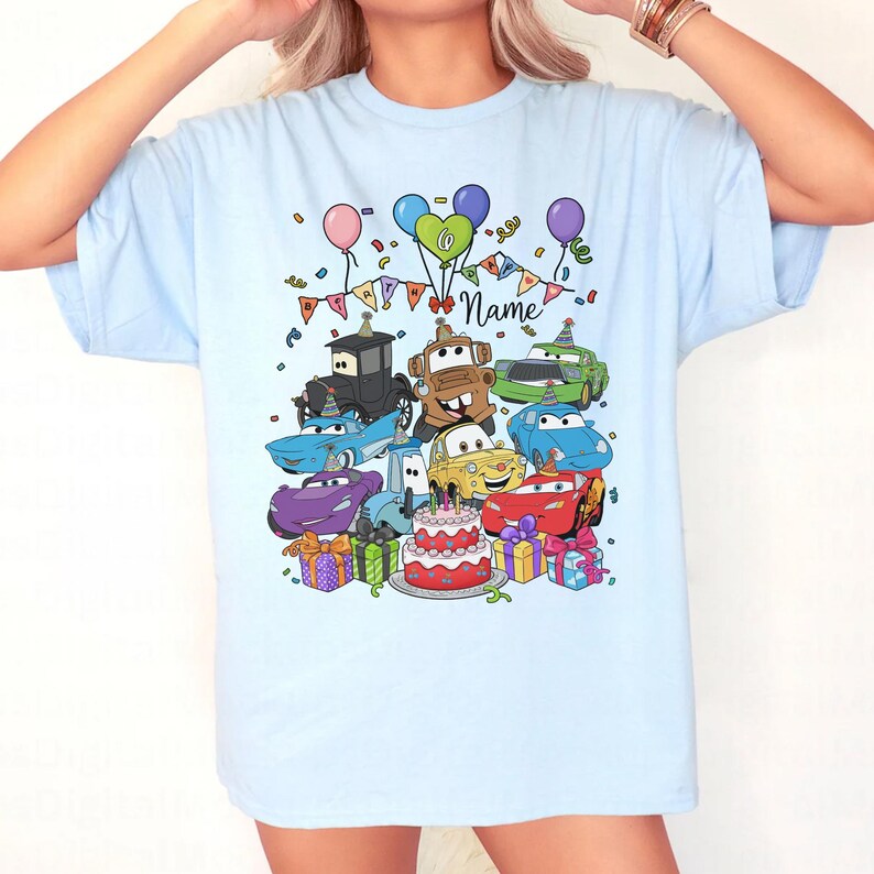 Peut inclure: T-shirt bleu clair avec un motif color&eacute; de voitures de dessins anim&eacute;s, un g&acirc;teau d'anniversaire, des ballons et des confettis. Le motif comprend le mot "Name" en &eacute;criture manuscrite, id&eacute;al pour la personnalisation. Un design festif et amusant.