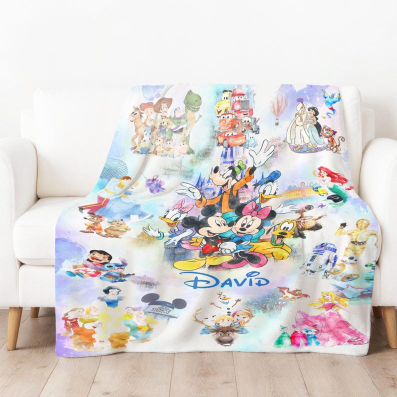 Op de afbeelding: Een witte fleece deken met een kleurrijk ontwerp van Disney-figuren, waaronder Mickey en Minnie Mouse, Donald Duck en personages uit Toy Story, Cars en Frozen. De naam "DAVID" is in blauw geschreven.