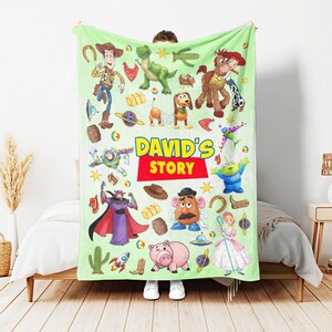 Puede incluir: Una manta de forro polar de color verde claro con un patr&oacute;n repetitivo de personajes de Toy Story, incluyendo a Woody, Buzz Lightyear, Rex, Slinky Dog, Jessie, Bullseye, Mr. Potato Head y Hamm. El texto DAVID'S STORY est&aacute; impreso en el centro.