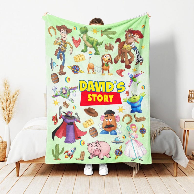 Puede incluir: Una manta de forro polar de color verde claro con un patr&oacute;n repetitivo de personajes de Toy Story, incluyendo a Woody, Buzz Lightyear, Rex, Slinky Dog, Jessie, Bullseye, Mr. Potato Head y Hamm. El texto DAVID'S STORY est&aacute; impreso en el centro.