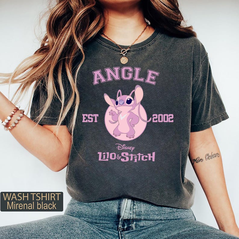 May include: Dark gray t-shirt featuring a pink cartoon character design with the text "ANGLE EST 2002" and "Disney Lilo & Stitch". The shirt also has the text "WASH TSHIRT Mirenal black".