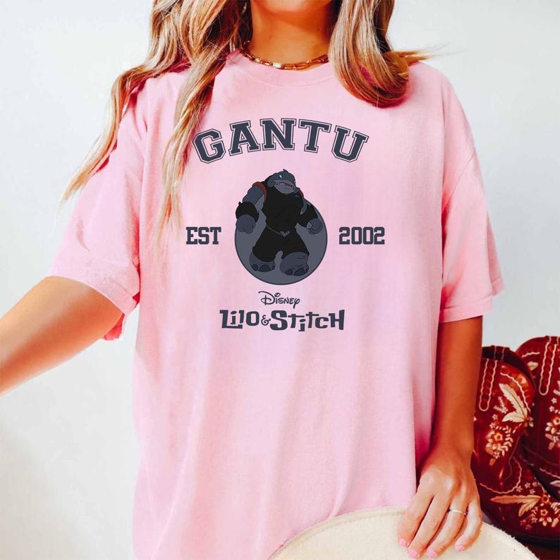 May include: Pink t-shirt featuring the word "GANTU" in navy blue arched text above a graphic of a character from Disney's Lilo & Stitch. The text "EST 2002" and "Disney Lilo & Stitch" are also printed on the shirt.