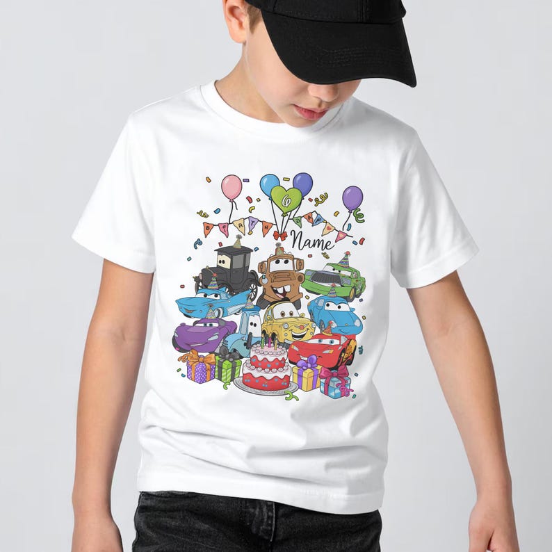 Peut inclure: T-shirt blanc avec un motif de voitures de dessins anim&eacute;s color&eacute;s sur le th&egrave;me d'un anniversaire. Le motif comprend divers personnages de voitures, des ballons, des confettis, un g&acirc;teau et le mot "Name".