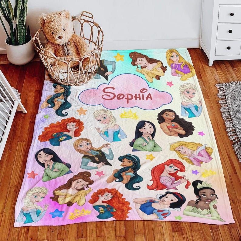 May include: A personalized blanket featuring various cartoon princesses in a colorful design. The blanket has a pink cloud with the name "Sophia" written in cursive. The princesses are surrounded by stars and crowns.