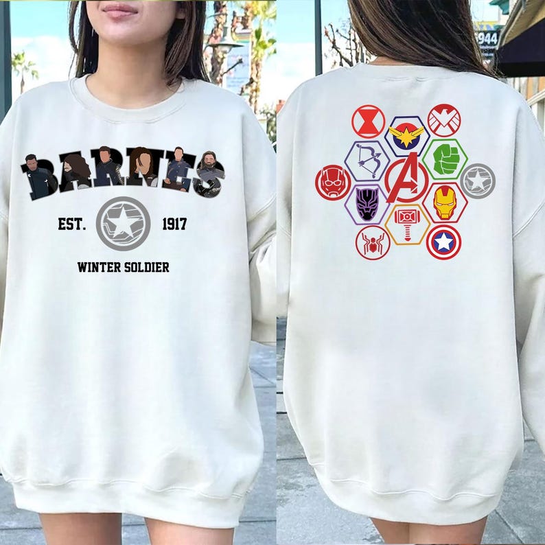 Puede incluir: Sudadera color crema con la palabra "BARTES" sobre "EST. 1917 WINTER SOLDIER" y un emblema de estrella. La parte trasera muestra s&iacute;mbolos de superh&eacute;roes y la letra "A" en un hex&aacute;gono, en un dise&ntilde;o colorido.