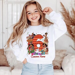 May include: A white long-sleeve sweatshirt featuring a large orange patterned number six surrounded by various animated characters in party hats, colorful gift boxes, and the text Custom Name printed in a red script font at the bottom.