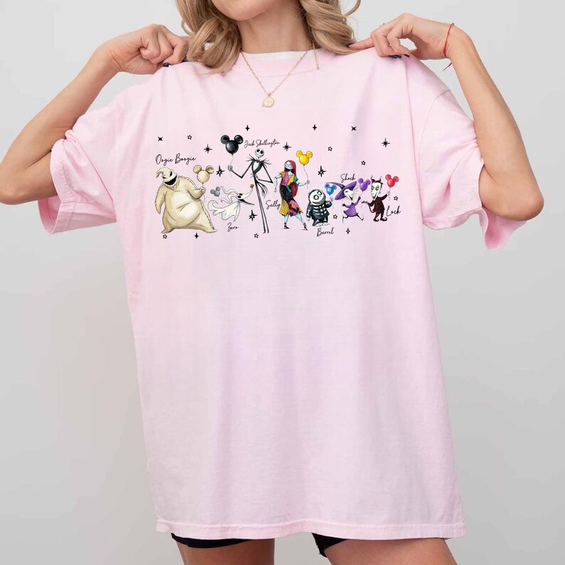 K&ouml;nnte beinhalten: Ein hellrosa T-Shirt mit einer Grafik von Charakteren aus The Nightmare Before Christmas. Die Charaktere sind Oogie Boogie, Jack Skellington, Sally und andere. Der Text "Oogie Boogie" und "Jack Skellington" sind ebenfalls sichtbar.