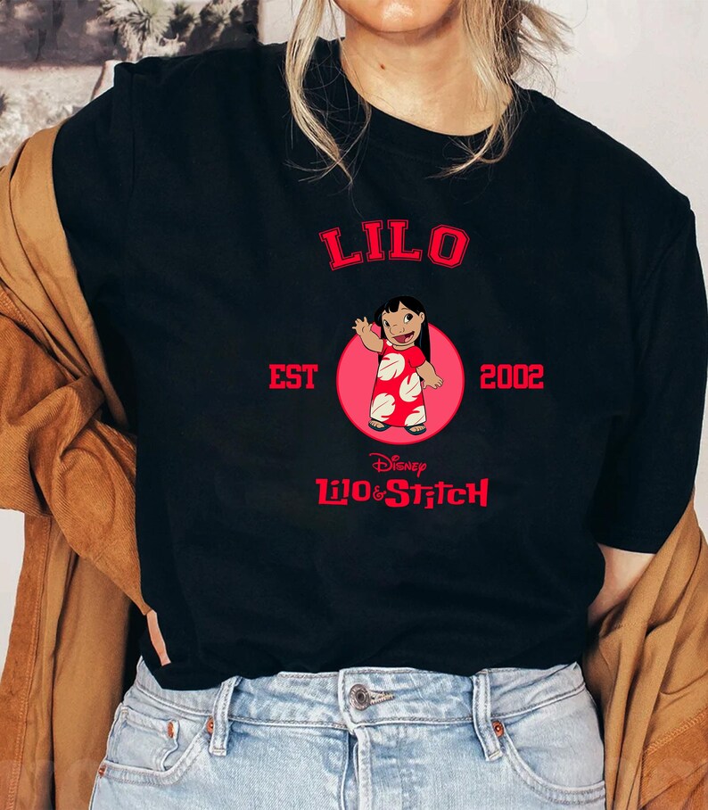 May include: Black t-shirt featuring a graphic of Lilo from Disney's Lilo & Stitch. The design includes the word "LILO" in red, the text "EST 2002", and the Disney logo. Lilo is depicted in a red dress with white spots, inside a pink circle.