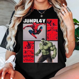 Op de afbeelding: Zwart T-shirt met stripboekillustraties van Spider-Man en Hulk, geplaatst in rode panelen. De bovenkant van het shirt toont de tekst "JUNPLAY", en het onderste linkerpaneel leest "BRAND NEW DAY".