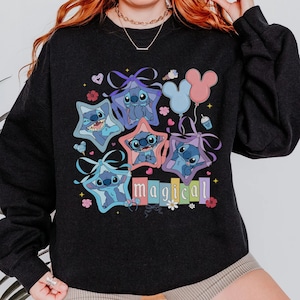 Może przedstawiać: Czarna bluza z kolorową grafiką postaci Stitch z Lilo & Stitch. Stitch jest przedstawiony w ramkach w kształcie gwiazd, z napisem "magical" poniżej. Balony i kwiatowe akcenty dopełniają projekt.