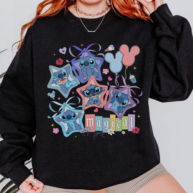 Może przedstawiać: Czarna bluza z kolorową grafiką postaci Stitch z Lilo & Stitch. Stitch jest przedstawiony w ramkach w kształcie gwiazd, z napisem "magical" poniżej. Balony i kwiatowe akcenty dopełniają projekt.