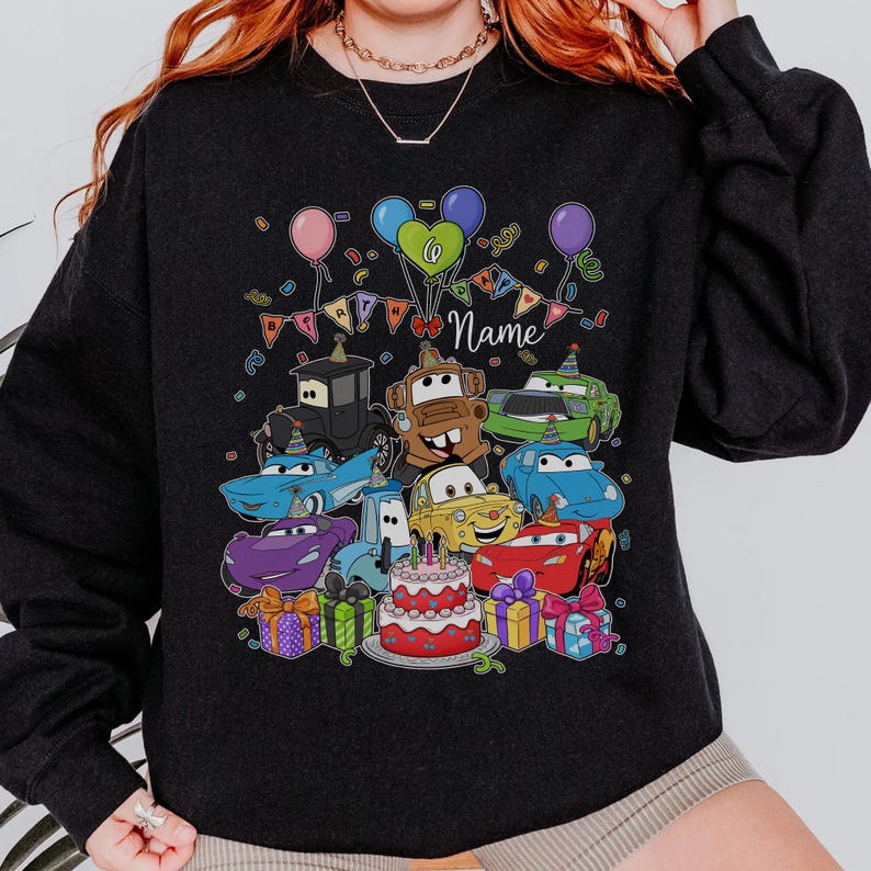 Peut inclure: Sweat-shirt noir avec un motif d'anniversaire color&eacute;. Il pr&eacute;sente des voitures de dessins anim&eacute;s, des ballons, des confettis, un g&acirc;teau et des cadeaux emball&eacute;s. Le mot "Name" est &eacute;crit en cursive. Un design festif pour une f&ecirc;te d'anniversaire.
