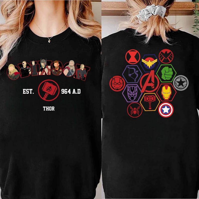 Puede incluir: Sudadera negra con un dise&ntilde;o que presenta la palabra "Thor", el texto "EST. 964 A.D." e ilustraciones de personajes. La parte trasera de la sudadera muestra varios s&iacute;mbolos de superh&eacute;roes y la letra "A" en el centro.
