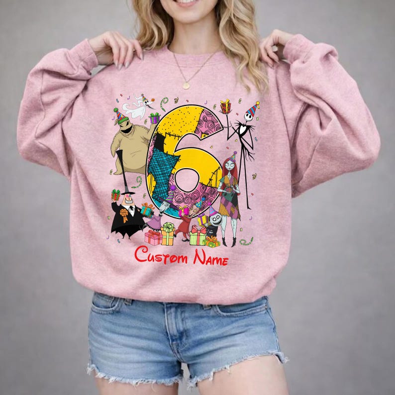 May include: A light pink crewneck sweatshirt featuring a large yellow number six graphic surrounded by characters from The Nightmare Before Christmas, including Jack Skellington, Sally, and Oogie Boogie, with the red text Custom Name below.