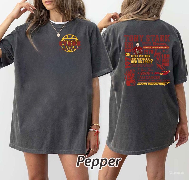 May include: Dark gray t-shirt with a graphic on the front and back. The front features a yellow and red design. The back has red text that reads "Tony Stark" and "Stark Industries". The shirt is a comfortable, casual style.