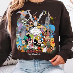 Puede incluir: Sudadera marr&oacute;n oscuro con un gr&aacute;fico colorido de varios personajes de Disney, incluyendo Mickey Mouse, Minnie Mouse y Winnie the Pooh. El texto "Magic Kingdom Walt Disney World" est&aacute; impreso en la parte inferior.