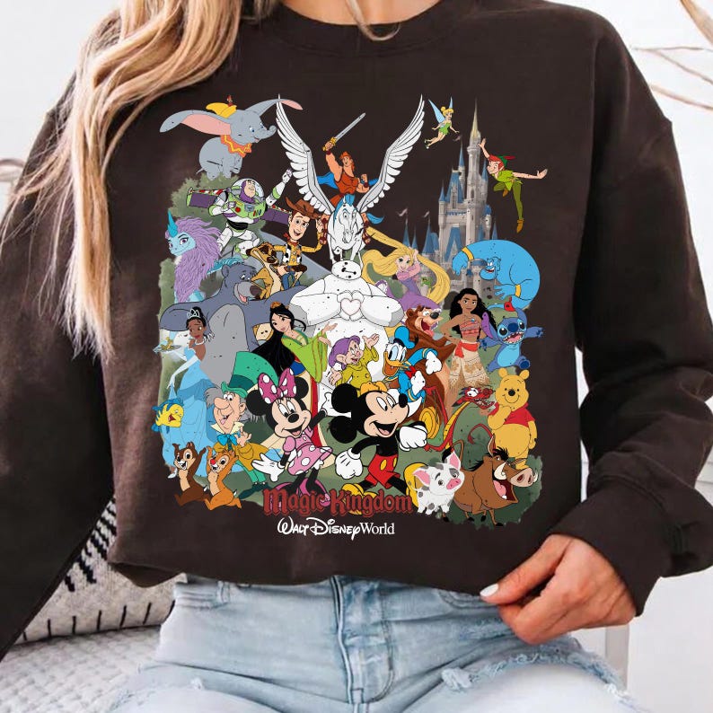 Puede incluir: Sudadera marr&oacute;n oscuro con un gr&aacute;fico colorido de varios personajes de Disney, incluyendo Mickey Mouse, Minnie Mouse y Winnie the Pooh. El texto "Magic Kingdom Walt Disney World" est&aacute; impreso en la parte inferior.