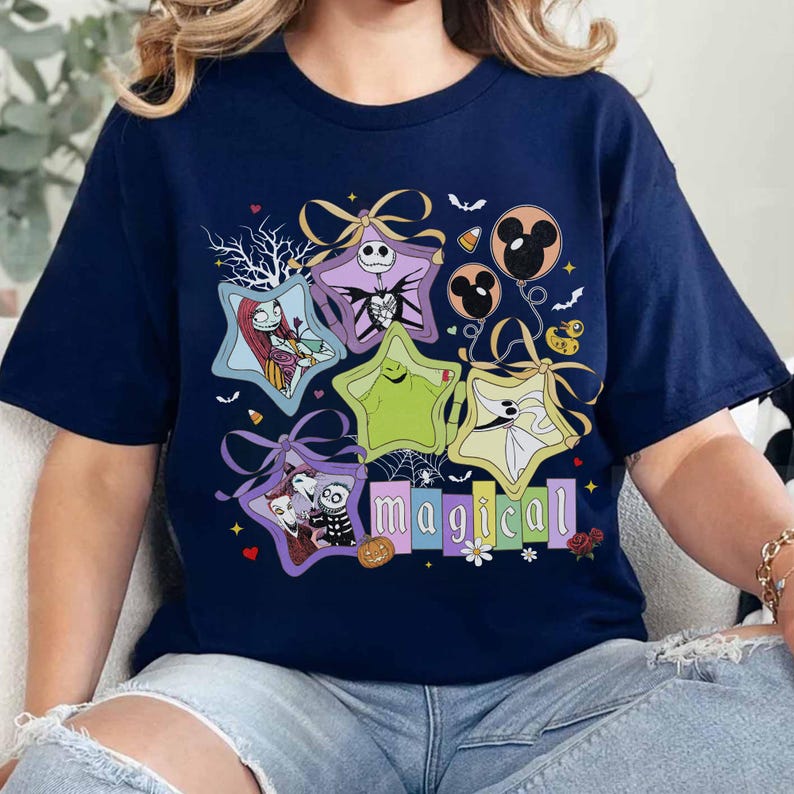 May include: Navy blue t-shirt with a colourful graphic design featuring characters from The Nightmare Before Christmas. The word "magical" is displayed in colourful block letters. The design includes stars, bows, and Halloween elements.