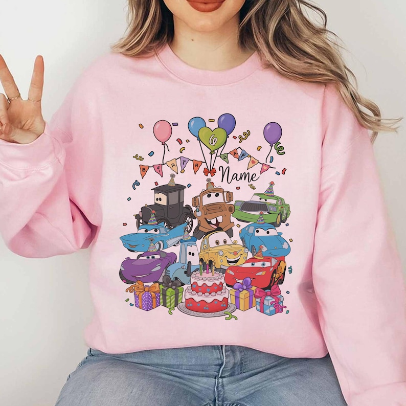 Peut inclure: Sweat-shirt rose clair avec un motif color&eacute; de voitures de dessins anim&eacute;s, un g&acirc;teau d'anniversaire, des ballons et des confettis. Le mot "Name" est &eacute;crit en cursive. Des cadeaux sont &eacute;galement inclus dans le design. Un design amusant et festif.
