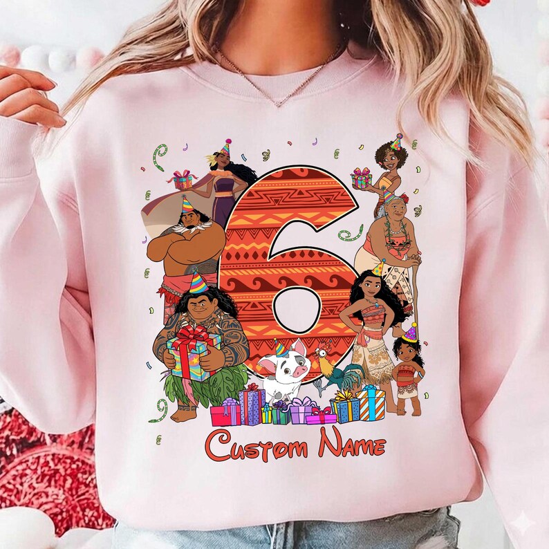 May include: A light pink crewneck sweatshirt featuring a large orange patterned number six surrounded by various animated characters from the movie Moana, including Moana, Maui, Pua, and Heihei, all wearing party hats with gift boxes and the text Custom Name.