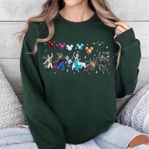 May include: Dark green sweatshirt featuring characters from a popular animated movie. The design includes illustrations of characters holding balloons with Mickey Mouse ears. Names of the characters are written above them.