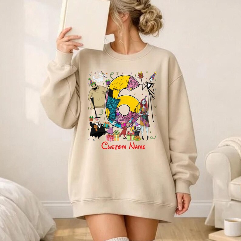 May include: A beige crewneck sweatshirt featuring a large graphic of the number six decorated with patterns, surrounded by various animated characters from The Nightmare Before Christmas, colorful gift boxes, and the red text Custom Name.