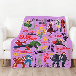 May include: A lavender throw blanket featuring various superhero characters and the name "William" in multiple fonts and colors. The blanket showcases illustrations of superheroes like Spider-Man, Hulk, and Captain America, among others. The design includes stars and the letter "W".